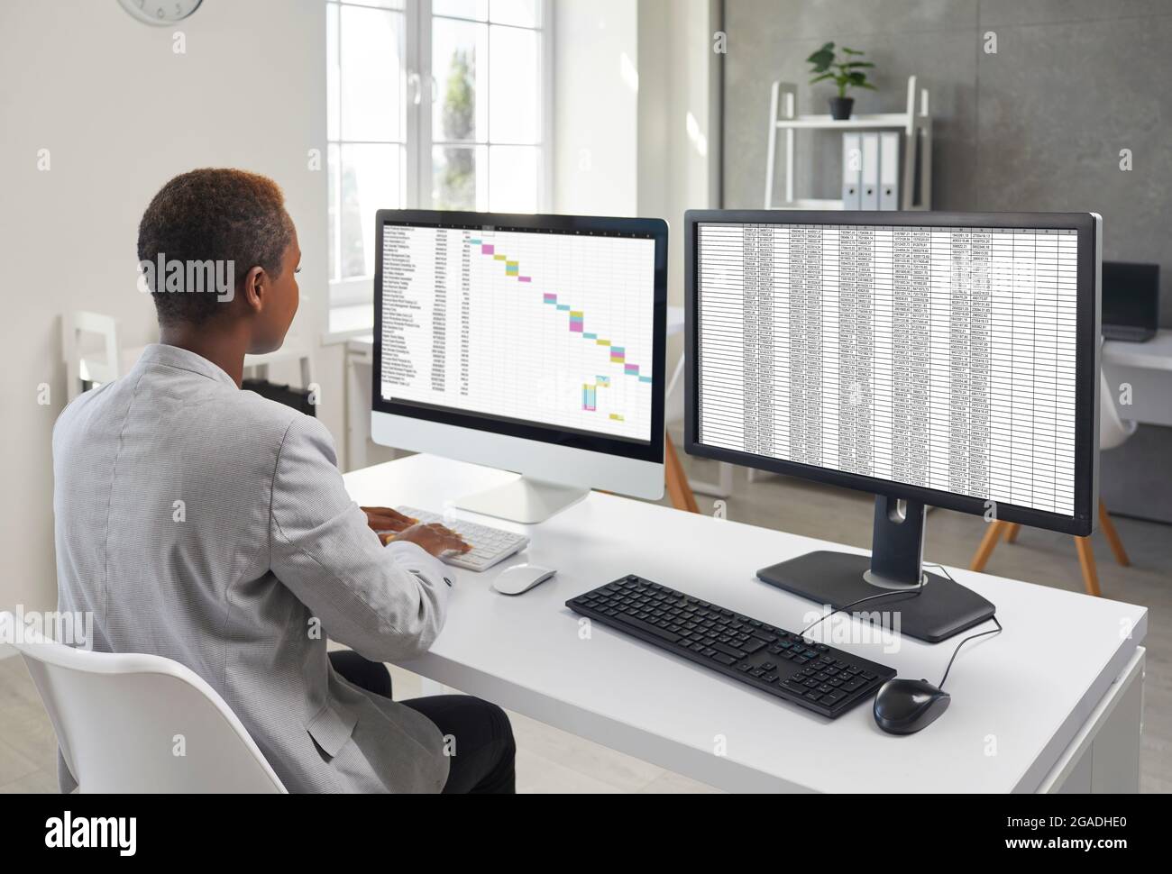 Finanzbuchhalter sitzt am Schreibtisch und arbeitet an zwei Desktop-Computern Stockfoto