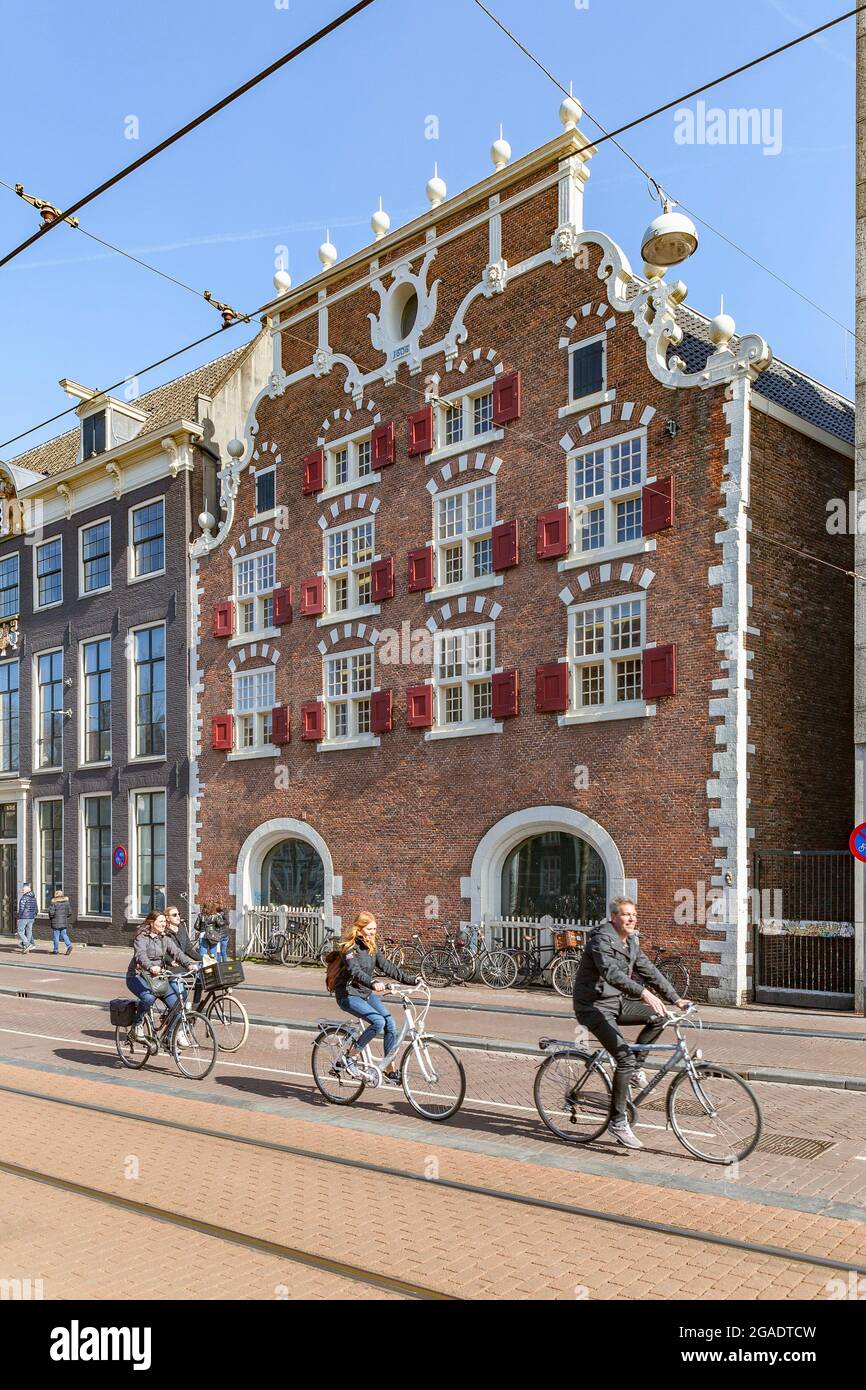 Radfahrer fahren vorbei an Stads-Bushuis, dem ehemaligen Stadtarsenal und königlichen Ställen, die heute Teil der Universitätsbibliothek sind, Singel, Amsterdam, Holland Stockfoto