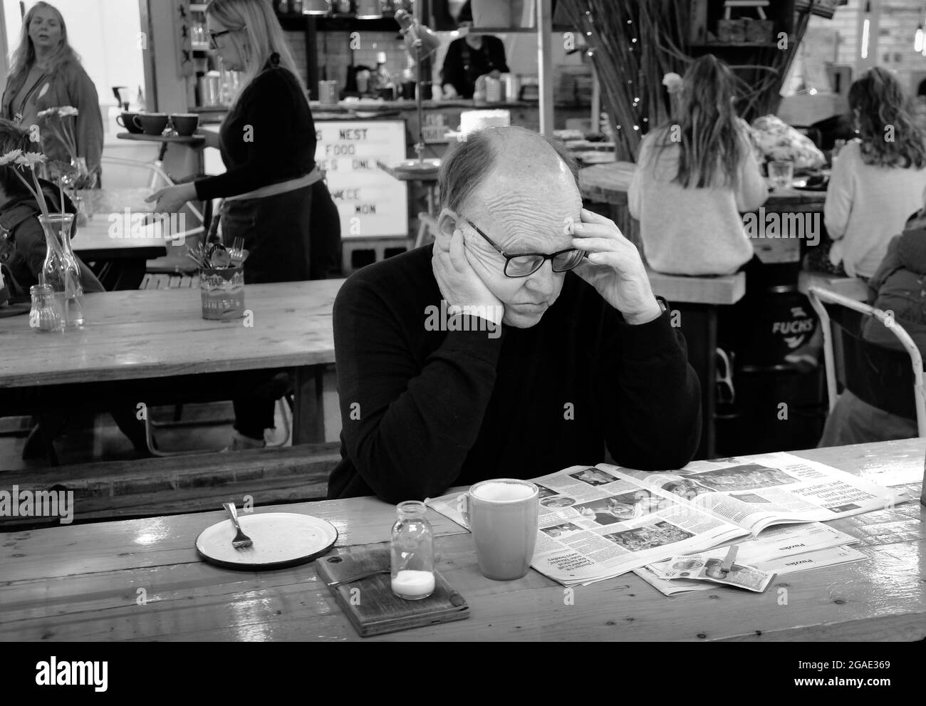 Ein älterer Mann sitzt in einem Café in Shrewsbury mit einer Tasse Kaffee. Er liest eine Zeitung. Monochrome Fotografie Stockfoto