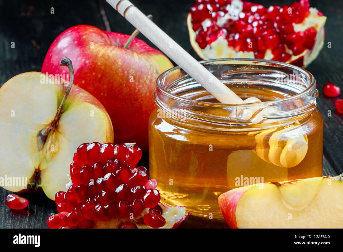 Jüdischer religiöser Feiertag Rosh Hashanah. Stillleben von Äpfeln, Granatäpfeln und Honig auf dunklem Holzgrund. Traditionelle Symbole der Feier Stockfoto