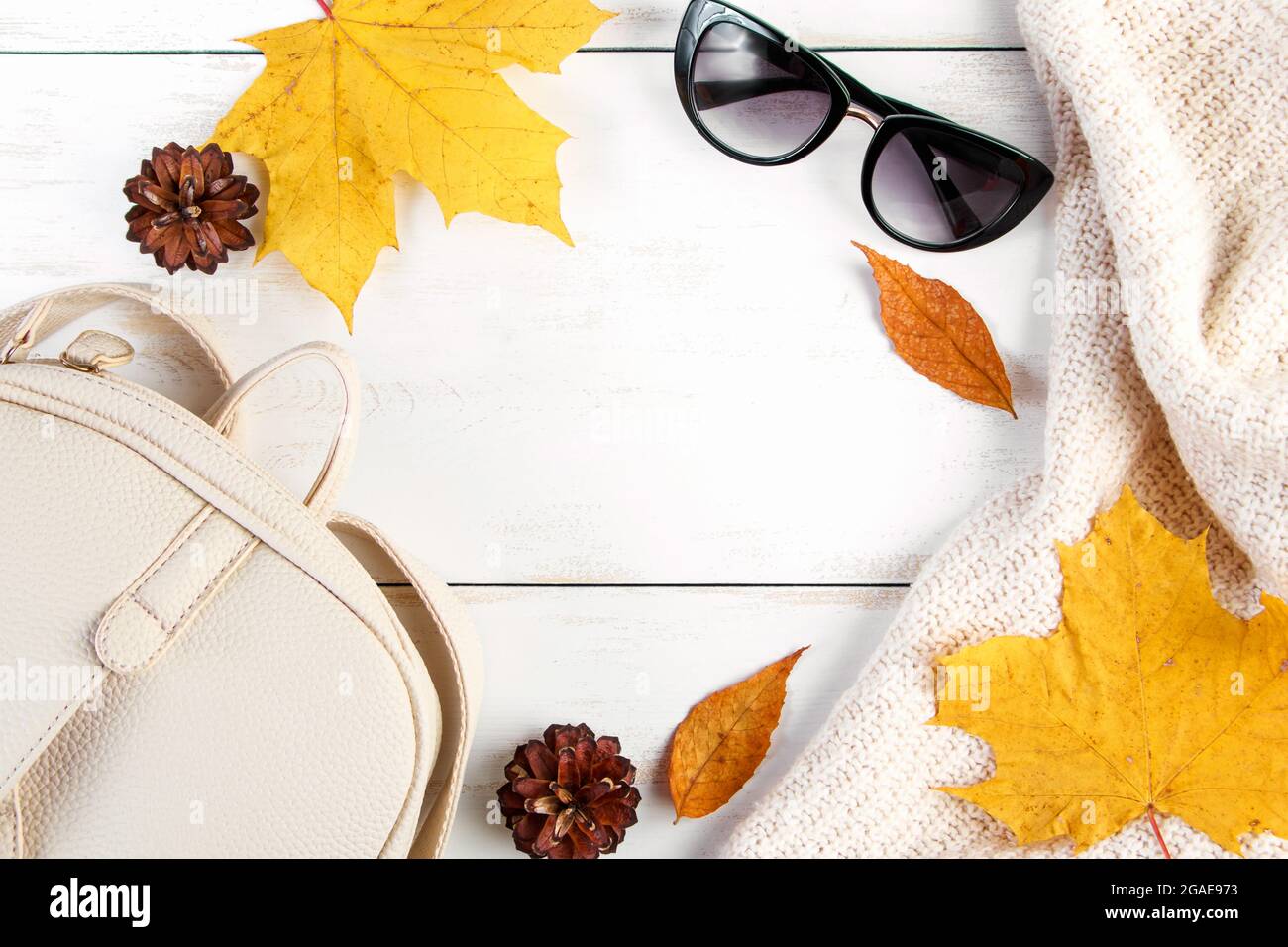 Hallo Herbst. Kreative flache Lay-Komposition auf weißem Hintergrund. Gelbe Blätter, Strickpullover, Rucksack und Brille. Speicherplatz kopieren. Stockfoto