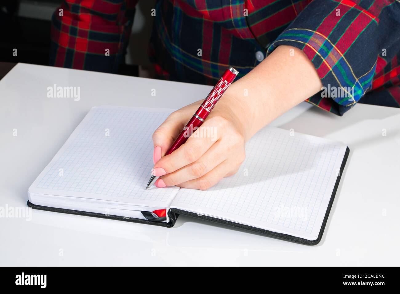 Die junge Frau hält einen Stift in der linken Hand und schreibt eine Notiz in ein leeres Notizbuch. Internationaler Tag Der Linken Stockfoto