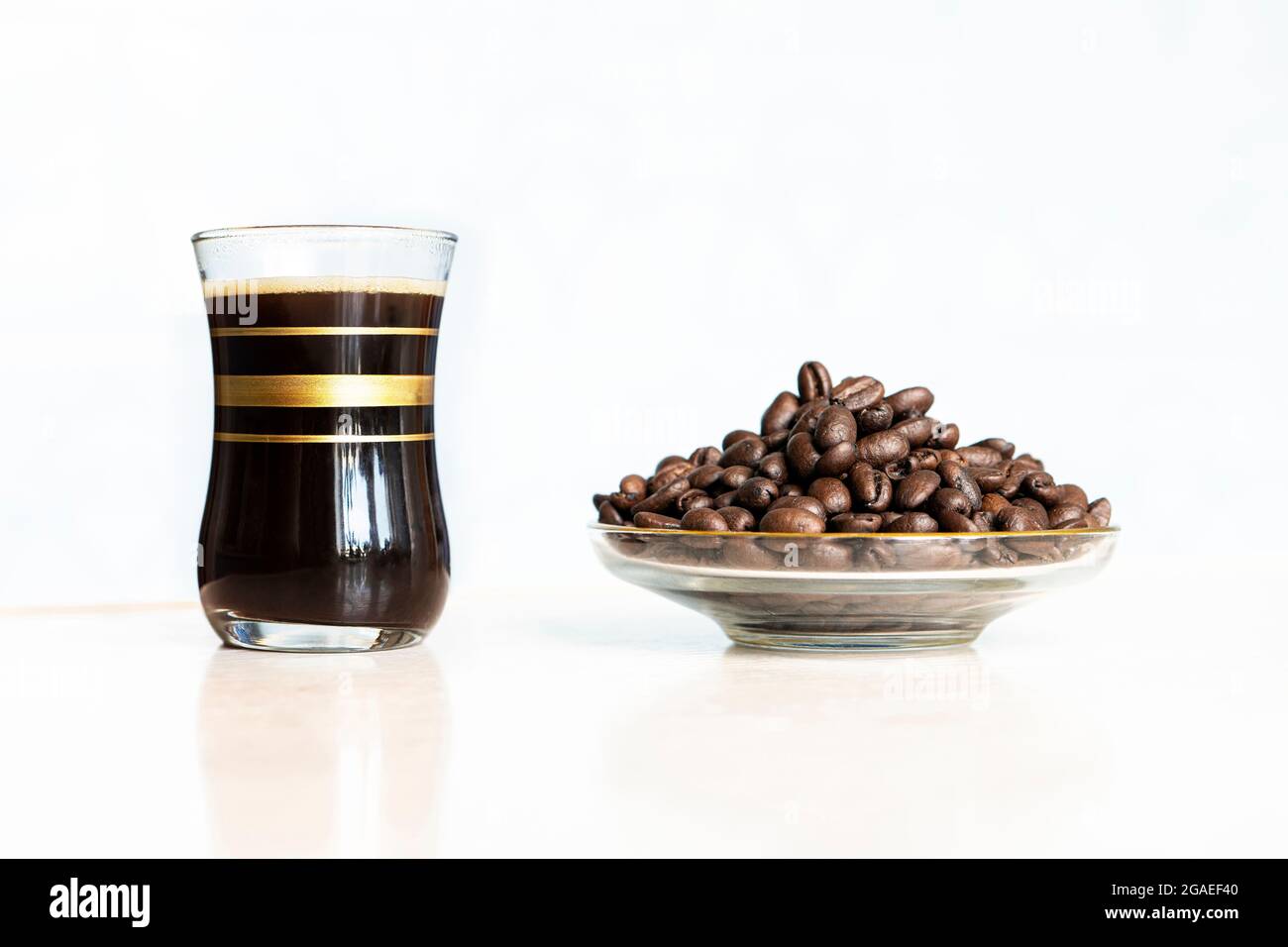Schwarzer Kaffee im Glas und geröstete Kaffeebohnen auf Holztisch auf weißem Hintergrund Stockfoto