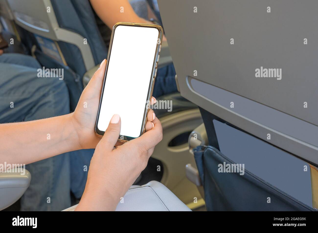 Frau, die im Flugzeug sitzt und ein Handy mit Mockup verwendet. Frau mit Smartphone im Flugzeug während des Fluges. Mockup Bild von Frauen Hände halten ein b Stockfoto