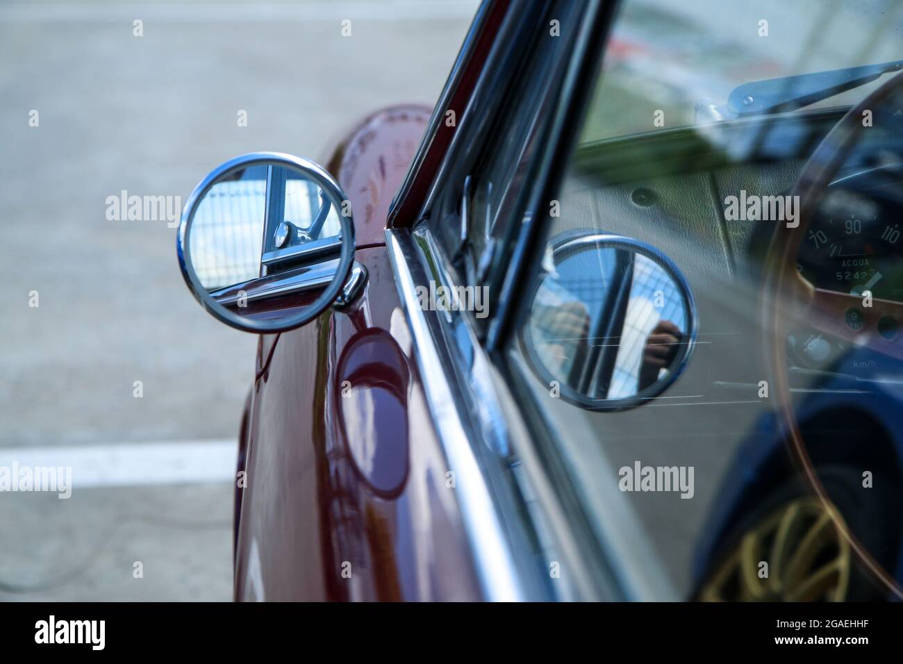 Das Detail des einfachen kleinen runden Seitenspiegels am klassischen italienischen Auto. Chrom und glänzend. Stockfoto