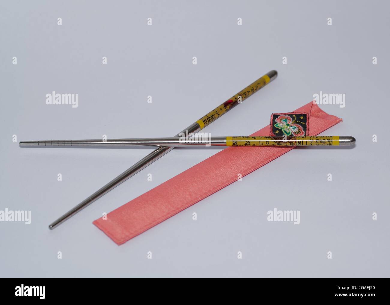 Ein Paar Essstäbchen aus Metall mit einem rosafarbenen Leinwandhalter Stockfoto