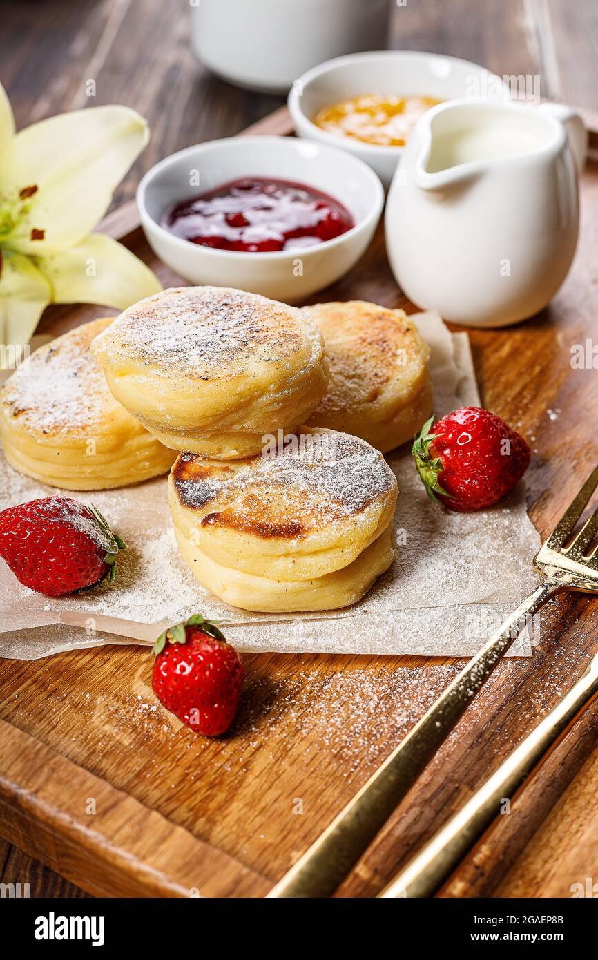 Quark-Pfannkuchen mit frischen Erdbeeren und Marmelade. Quark Pfannkuchen auf einem Holzbrett mit Puderzucker bestreut. Köstliche hausgemachte Brea Stockfoto