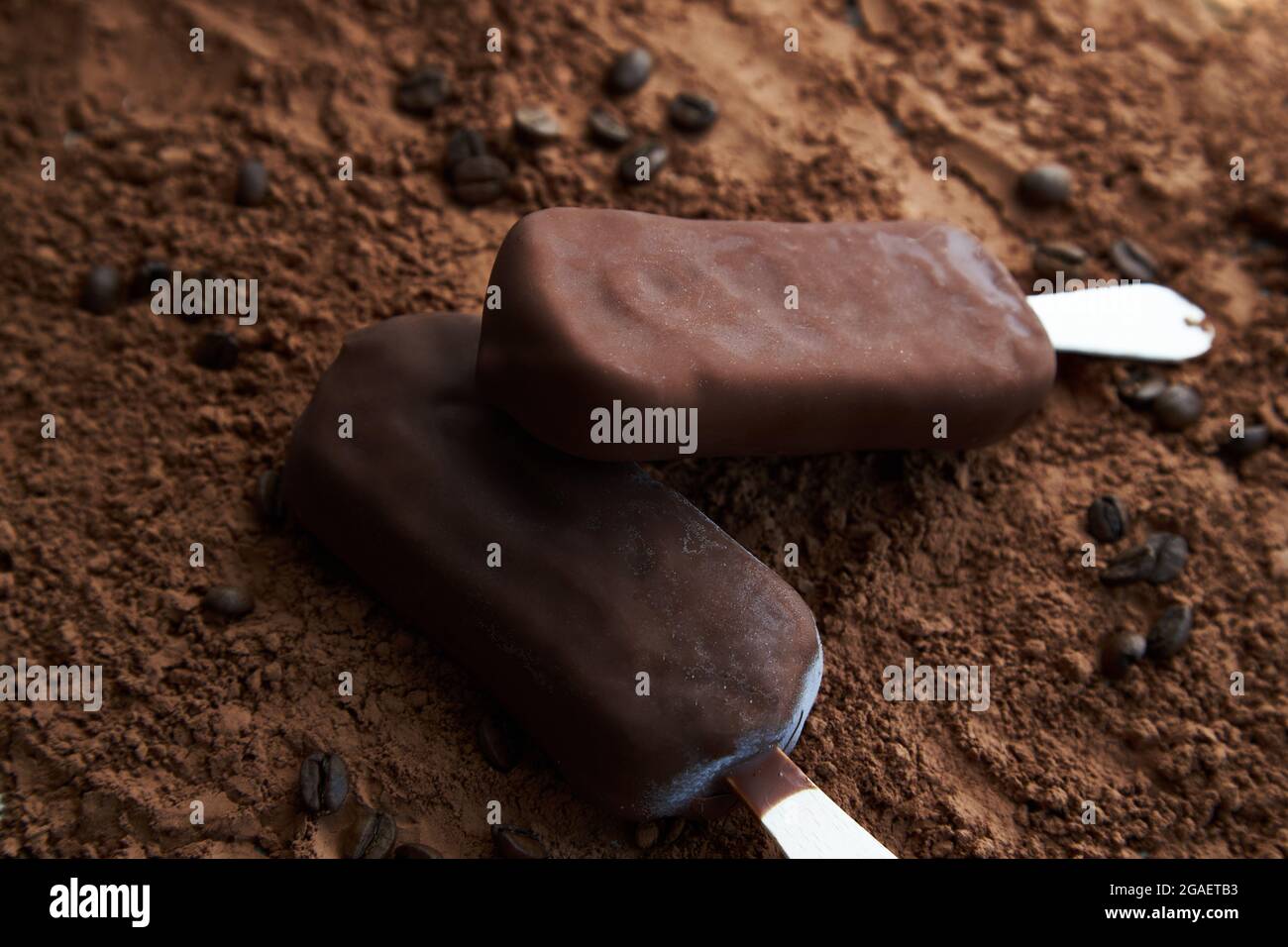 Zwei Schokoladenpopsicles auf einem strukturierten braunen Hintergrund aus Kakaopulver und Kaffeebohnen. Süßes Eis-Konzept für Design. Stockfoto
