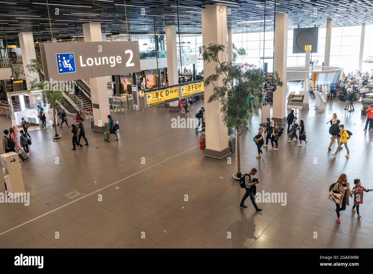 Amsterdam, Niederlande - 29. Juli 2021: Reisende wandern durch den Flughafen Shiphol. Vollständig geimpfte Reisende dürfen während einer Pandemie reisen, müssen aber auf Flughäfen und in Flugzeugen Masken tragen. Stockfoto