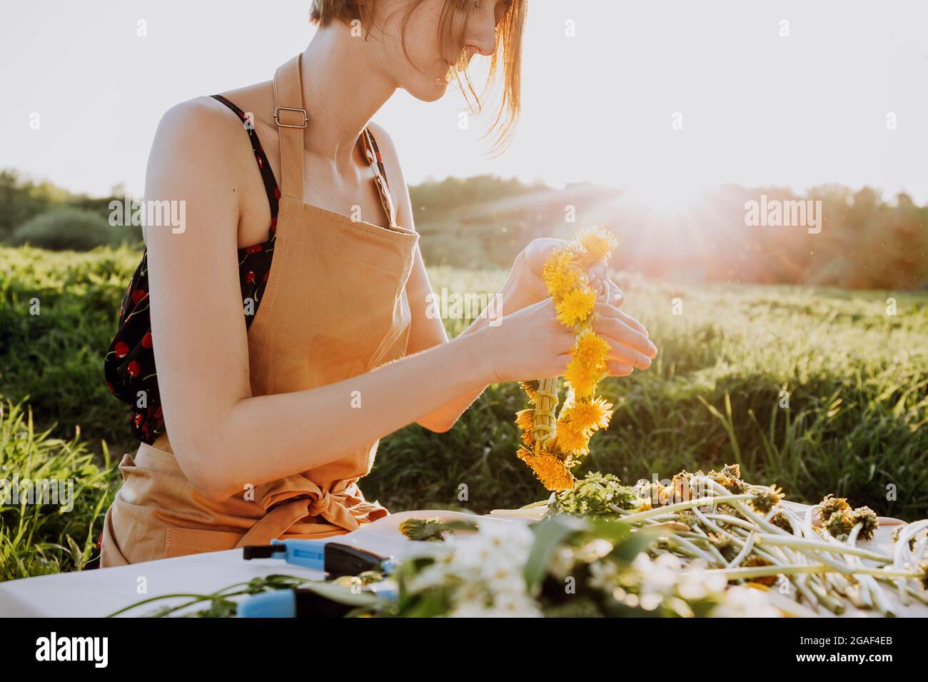 Floristen-Workshop. Hübsche Frau, die einen Kranz aus dem Dandelion macht. Romantischer Hintergrund des Floristen bei der Arbeit Stockfoto