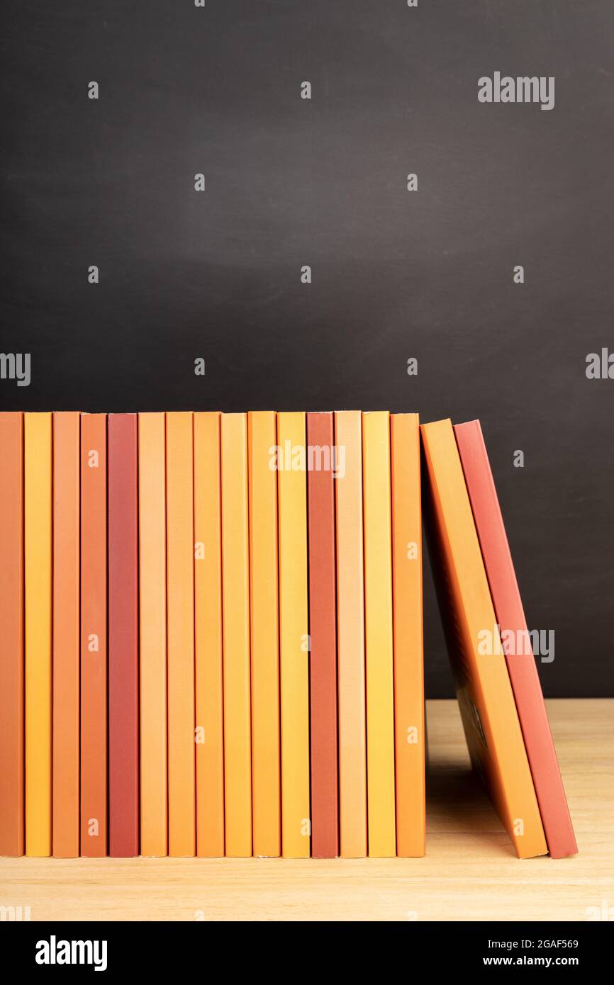Gruppe von orangefarbenen Büchern auf Holztisch oder Regalen und Tafel im Hintergrund. Speicherplatz kopieren Stockfoto