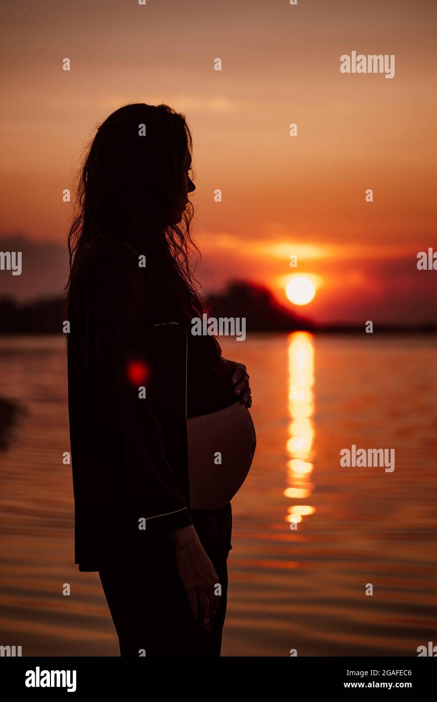 Silhouette Einer Frau In Sonnenstrahlen Junge Schwangere Im Dunklen Anzug Und Nassem Langen Haar Steht Vor Dem Hintergrund Der Untergehenden Sonne Am Meer Stockfotografie Alamy