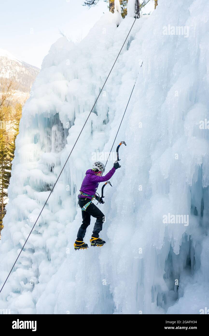 Low-Angle-Aufnahme einer alpinistischen Frau mit Eiskletterausrüstung, Axt und Kletterseilen, Klettern an einem gefrorenen Wasserfall, Blick von unten Stockfoto