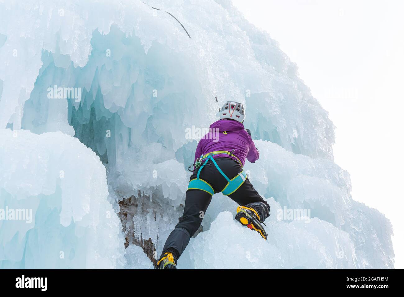 Eiskletterin klettert die Seite eines vereisten Hanges mit Unebenheiten, Graten und Eiszapfen hinauf Stockfoto