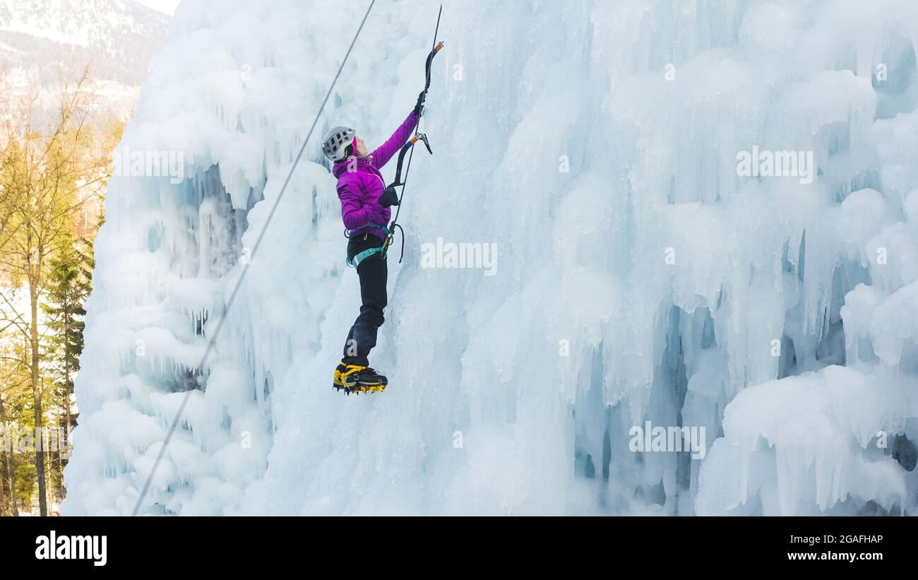 Weibliche Eiskletterin Silhouette schwingende Eisachsen auf ihrem Weg nach oben vertikalen Eiswasserfall, Seitenansicht Stockfoto