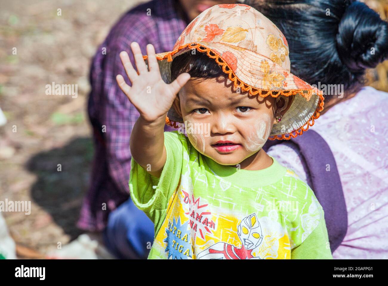 Niedliches junges burmesisches Kind mit Thanaka-Puder und Floppy-Sonnenhut-Wellen an der Kamera, Mine Thauk, Inle Lake, Myanmar Stockfoto