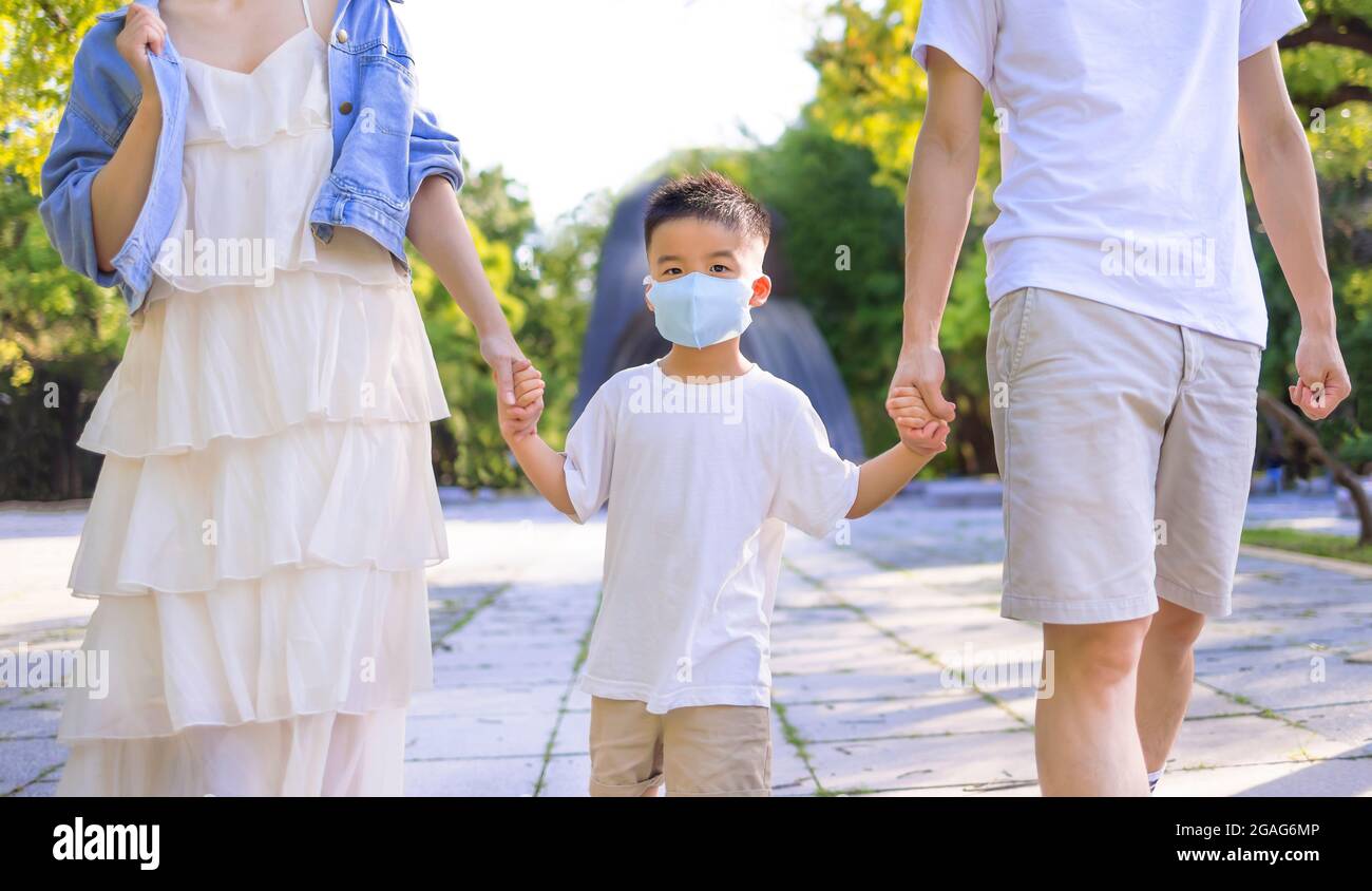 Glückliche Familie, die die medizinische Maske trägt und im Park spazierengeht. Stockfoto
