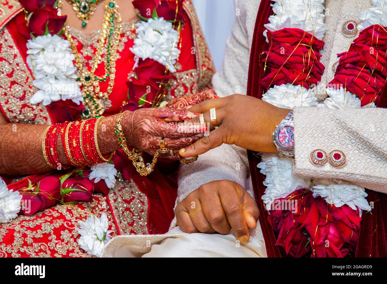 Die Braut mit Brautschmuck und Henna-Dekoration auf der Hand befestigt den Ring am Finger des Bräutigams bei der traditionellen religiösen Zeremonie bei einer hinduistischen Hochzeit Stockfoto