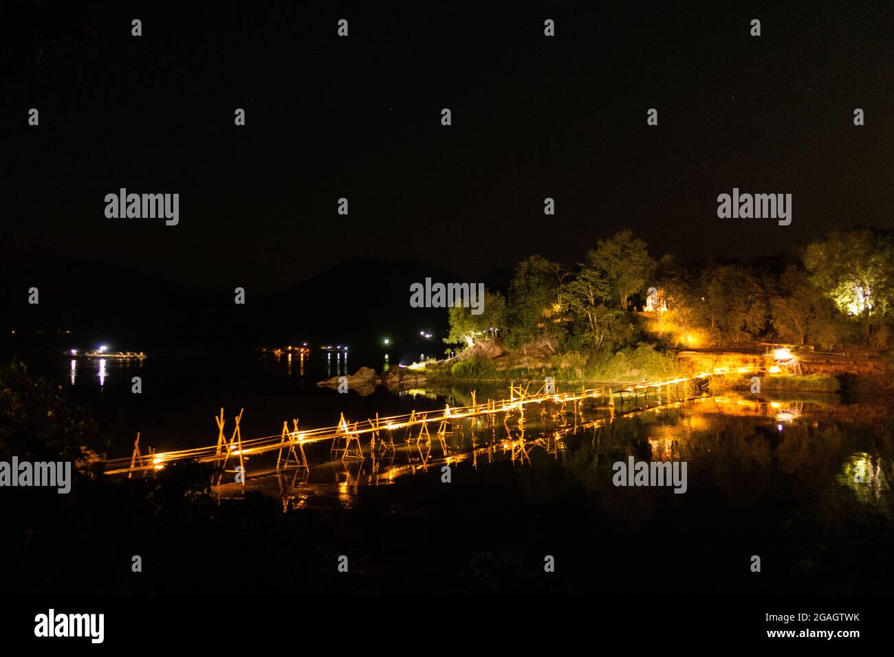 Hölzerne Bambusbrücke mit wunderschöner dekorativer Beleuchtung am Abend, die den Nam Khan Fluss in Luang Prabang, Laos, überquert. Stockfoto
