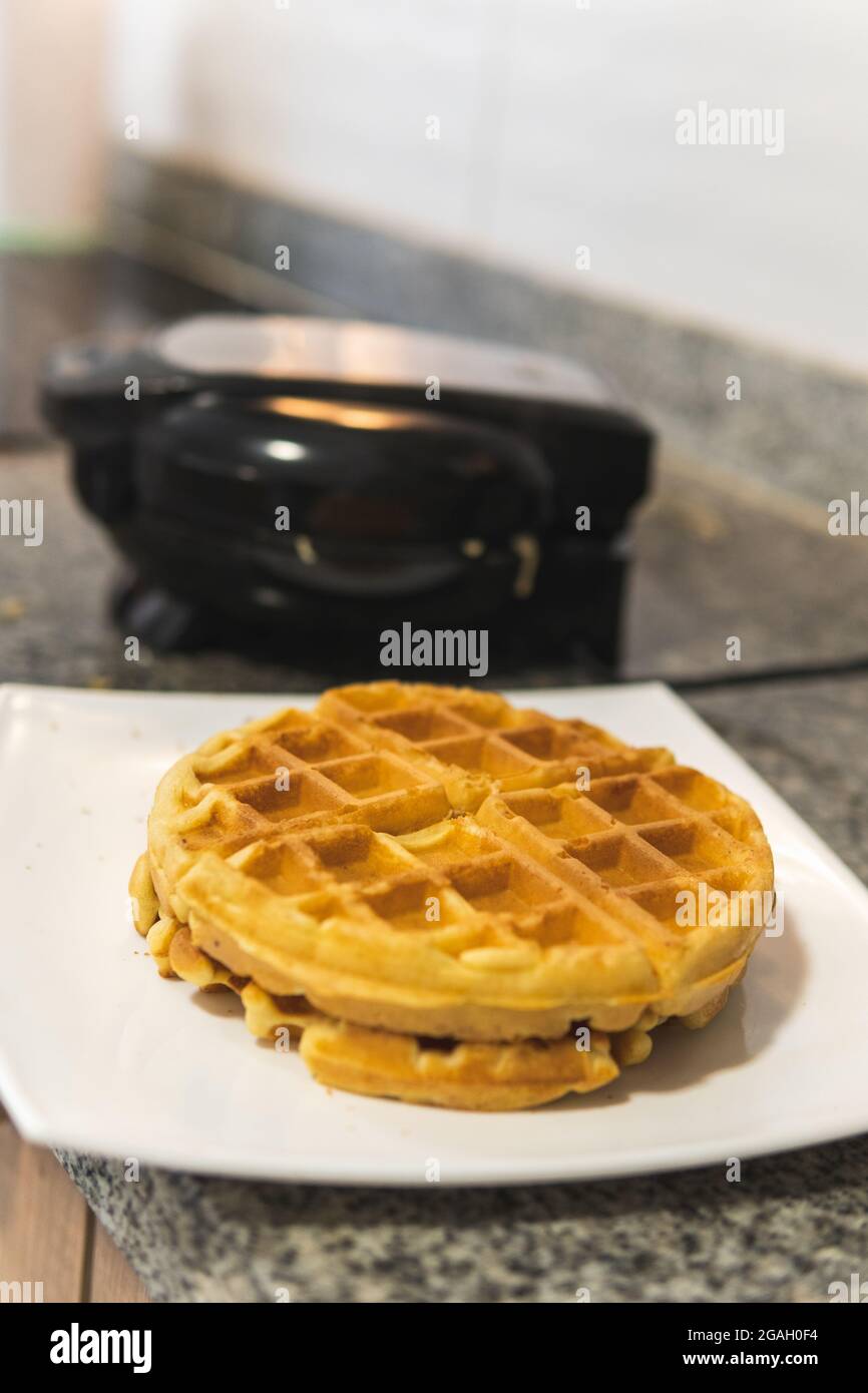 Nahaufnahme von goldenen Waffeln mit dem Waffeleisen im Hintergrund. Stockfoto