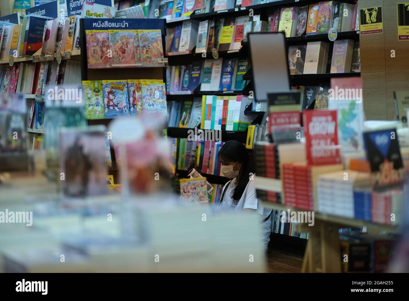 Die junge Thailänderin liest ein Buch in einem bequemen, schweren Bücherregal der öffentlichen Bibliothek oder einer Buchhandlung Stockfoto