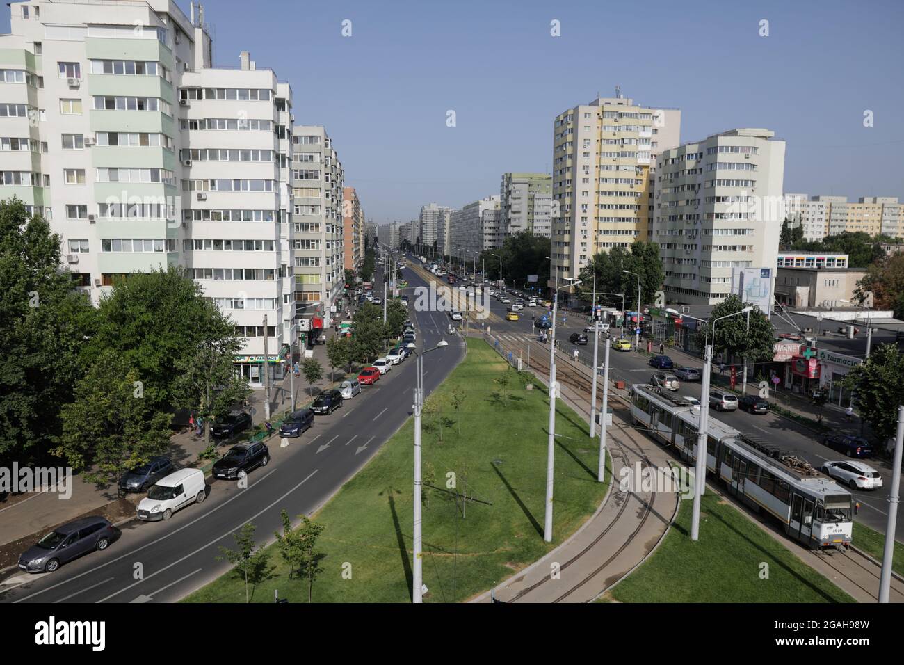 Bukarest, Rumänien - 29. Juli 2021: Autos und Fußgänger fahren auf einer belebten Straße von Bukarest mit Wohnblöcken aus der kommunistischen Ära an den Seiten. Stockfoto