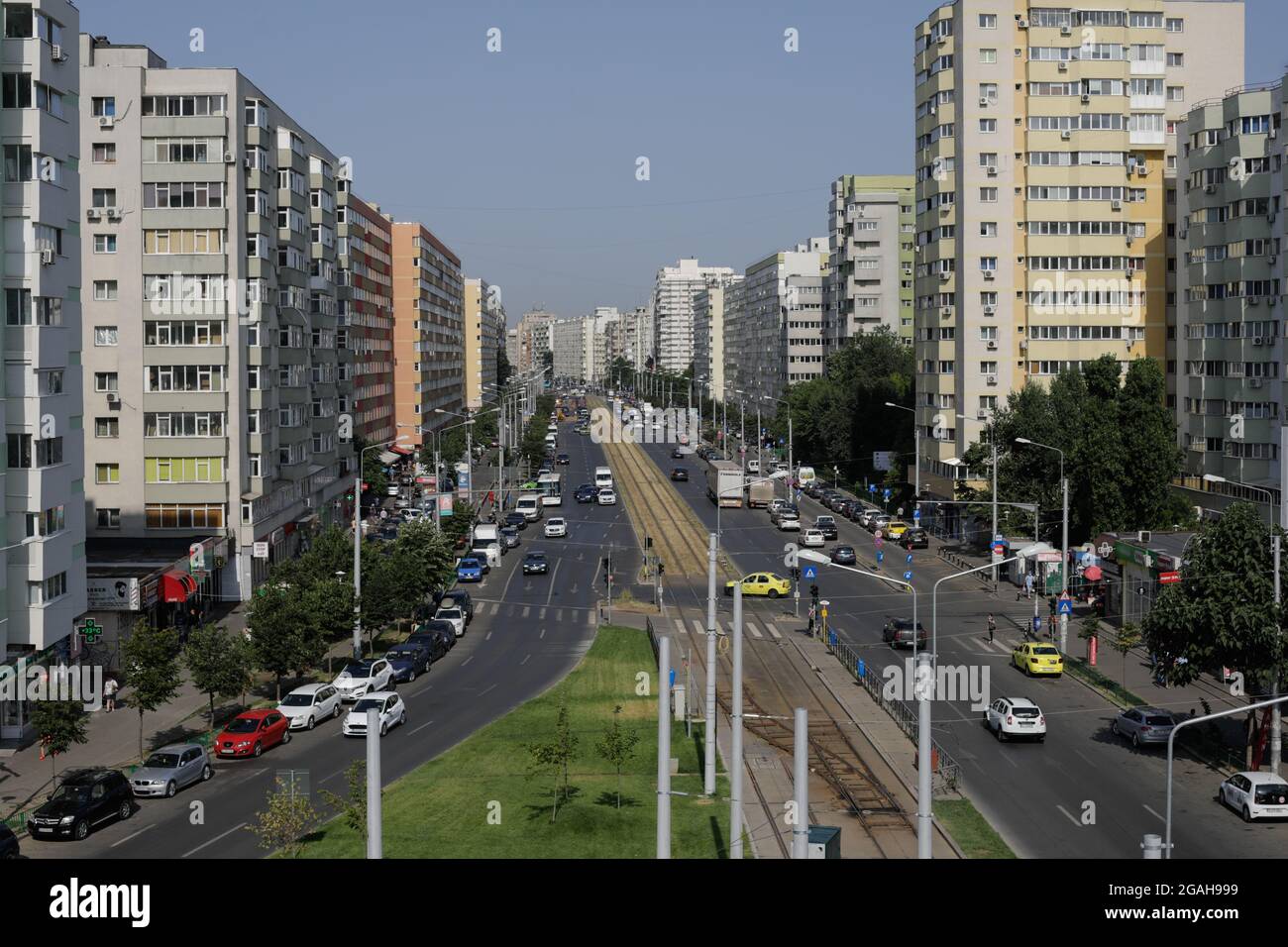 Bukarest, Rumänien - 29. Juli 2021: Autos und Fußgänger fahren auf einer belebten Straße von Bukarest mit Wohnblöcken aus der kommunistischen Ära an den Seiten. Stockfoto