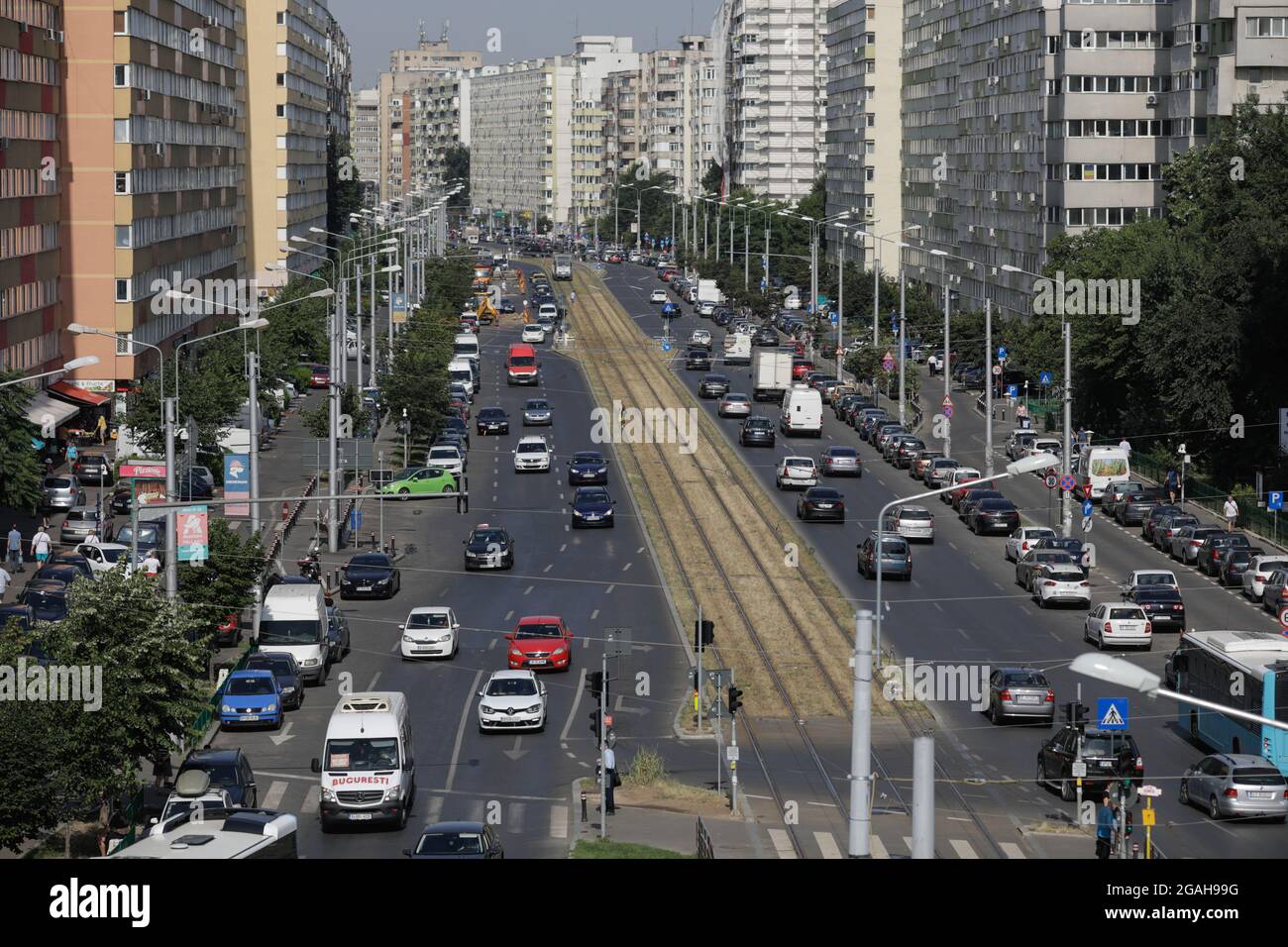 Bukarest, Rumänien - 29. Juli 2021: Autos und Fußgänger fahren auf einer belebten Straße von Bukarest mit Wohnblöcken aus der kommunistischen Ära an den Seiten. Stockfoto