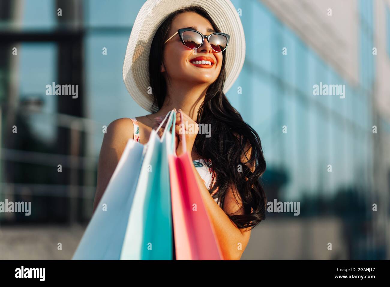 Junge, fröhliche Fashionista, die die Straße entlang geht, shopaholic mit Einkäufen in der Stadt vor dem Hintergrund der Vitrinen eines Einkaufszentrums, sh Stockfoto