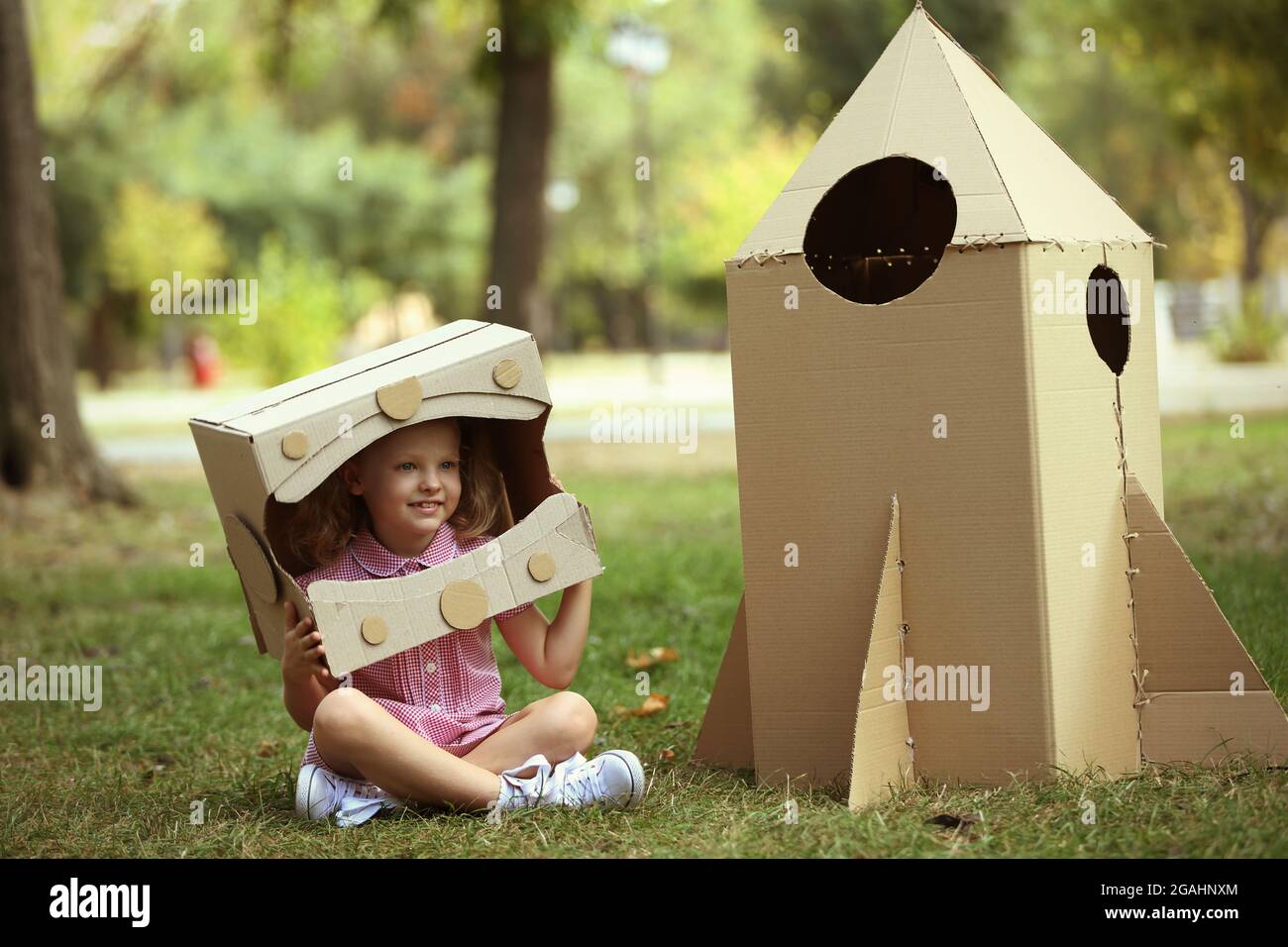 Kleine Mädchen in Karton Karton Helm in der Nähe der Rakete sitzen im Park  Stockfotografie - Alamy