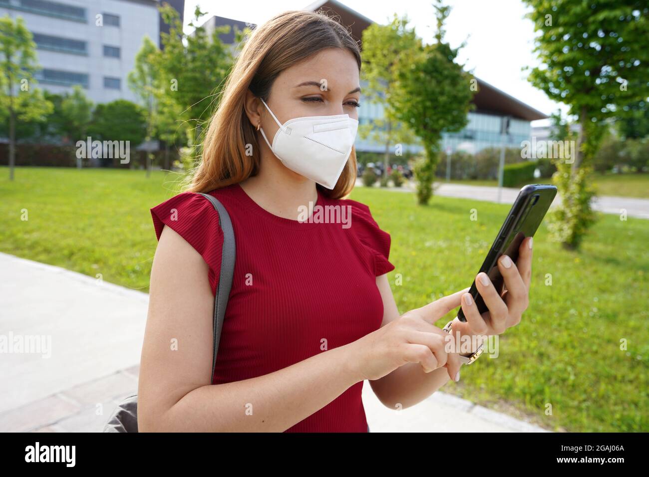 Bürgerin weiblich mit medizinischer Maske beobachten ihr Handy im Freien. Green-Pass- und Digital-Covid-Zertifikat-Konzept. Stockfoto