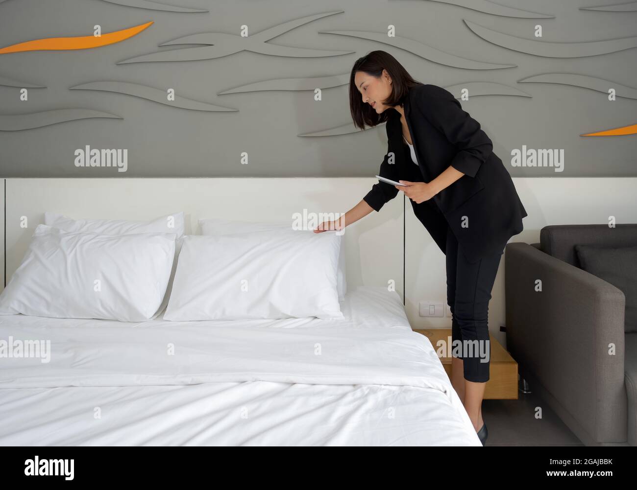 Asiatische Geschäftsfrau in schwarzem Anzug stehen mit Tablet-Computer in der Hand. Der Hotelmanager überprüft die Ordnung des Zimmers für Hotelgäste. Stockfoto