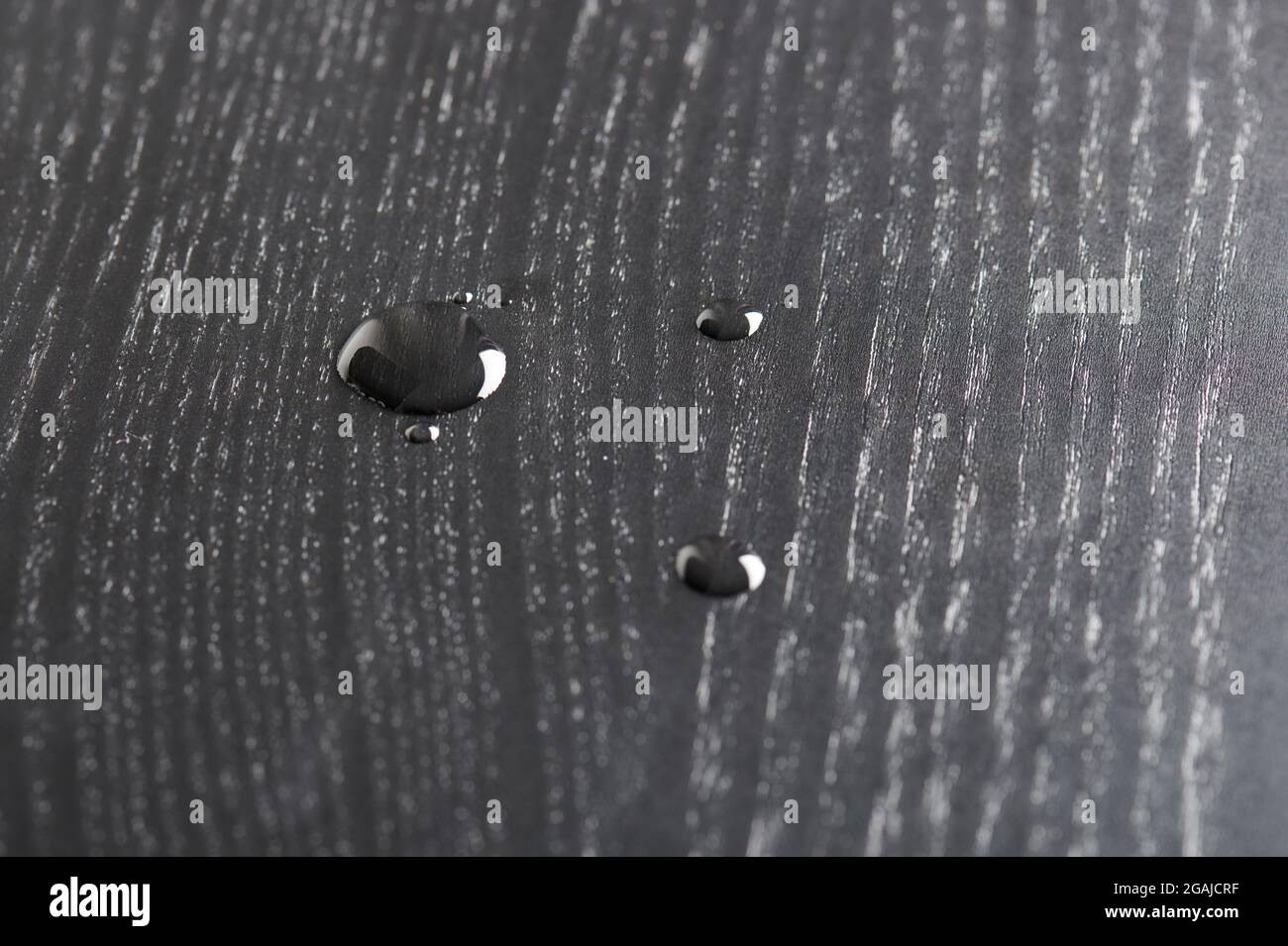 Wassertropfen auf schwarzer Holzoberfläche Makroansicht Stockfoto