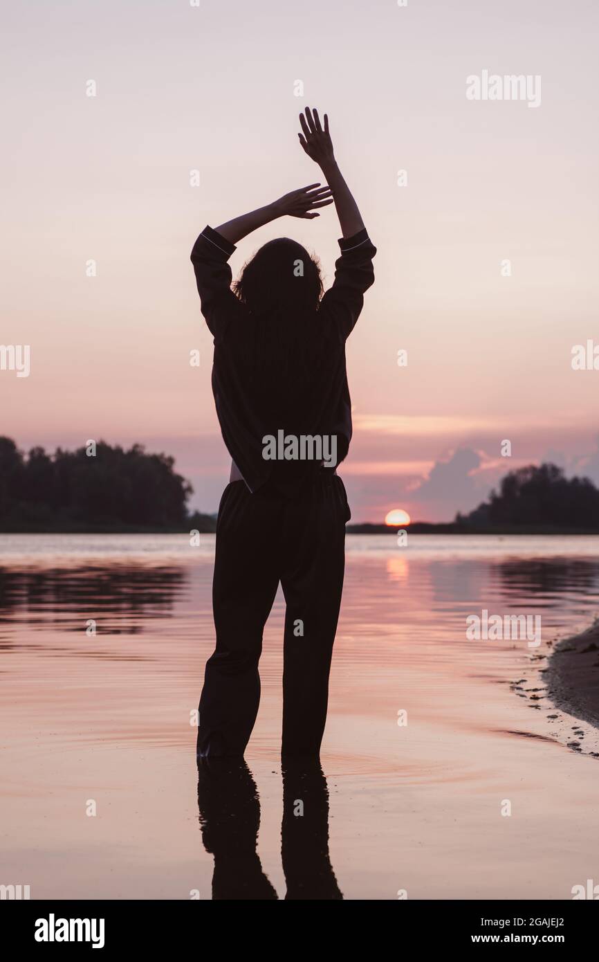 Silhouette Einer Frau Mit Erhobenen Handen Junge Schlanke Brunette Mit Langen Braunen Haaren In Schwarzem Anzug Steht Im Wasser Und Geniesst Meer Und Sonnenuntergang Stockfotografie Alamy