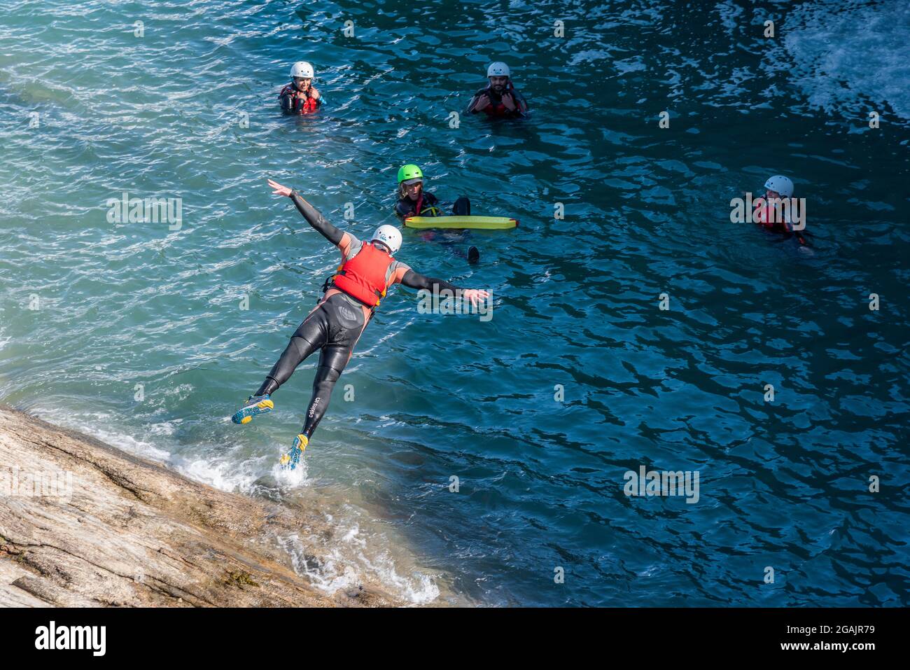 Urlauber, die mit ihrem kolenkenden Fremdenführer an der Küste von Towan Head in Newquay in Cornwall ins Meer springen. Stockfoto