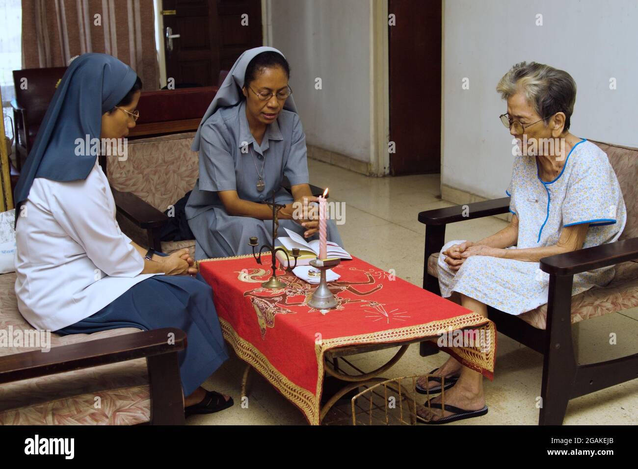 Zwei katholische Nonnen und eine alte Frau beten gemeinsam im Wohnzimmer. Stockfoto