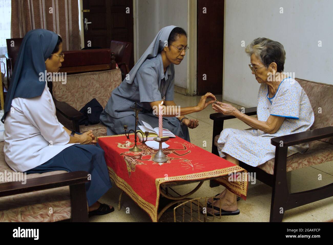Eine katholische Nonne gibt einer alten Frau in ihrem Haus ein sakramentales Brot (oder eine Gastgeberin). Stockfoto
