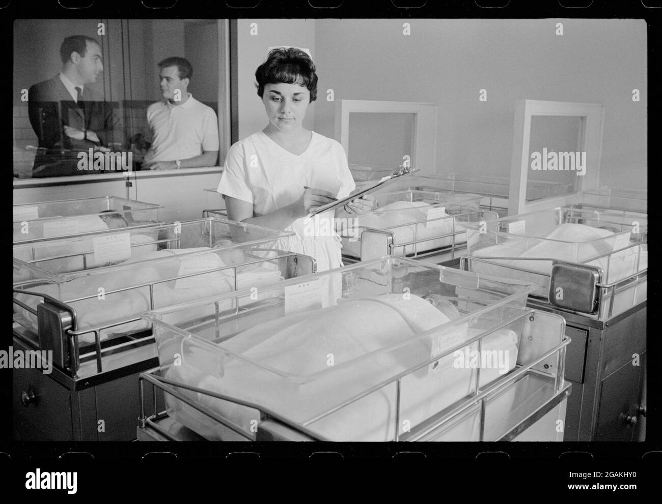 Krankenschwester pflegt Neugeborene im Kinderzimmer des Georgetown University Hospital, während stolze Väter am Sichtfenster stehen, Washington, DC, 9/23/1964. (Foto von Marion S Trikosko/US News & World Report Collection/RBM Vintage Images) Stockfoto