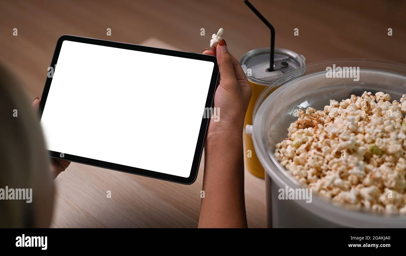 Junge Frau, die sich Online-Filme auf einem digitalen Tablet ansieht und zu Hause Popcorn auf dem Sofa isst. Stockfoto