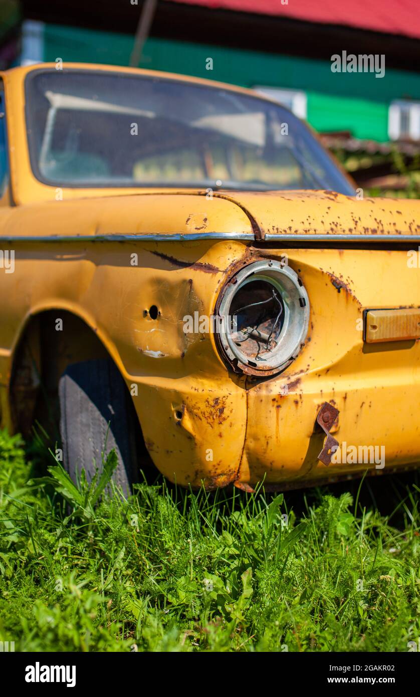 Altes gelbes Wrackauto im Vintage-Stil. Verlassene rostige gelbe Auto. Nahaufnahme der Scheinwerfer der Vorderansicht eines rostigen, gebrochenen, verlassenen Autos nea Stockfoto