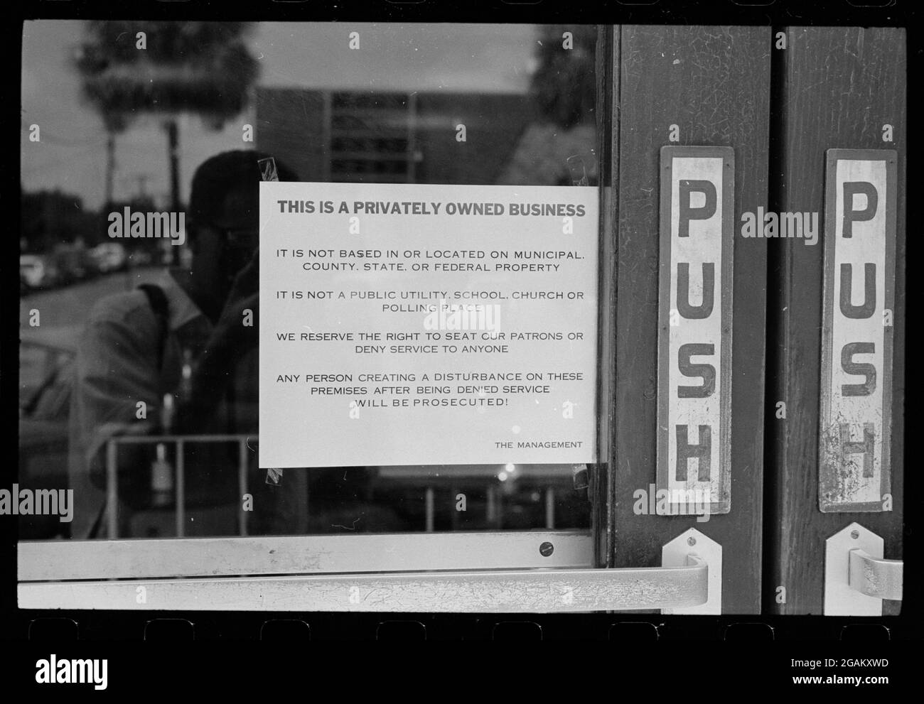 Schild an der Tür eines Restaurants, das vor dem Recht des Unternehmens warnt, jedem Gast den Service zu verweigern. Afroamerikaner, die das Zeichen der Segregation-Ära fotografieren, spiegeln sich im Glas wider, Albany, GA,8/18/1962. (Foto von Warren K Leffler/US News & World Report Collection/RBM Vintage Images) Stockfoto