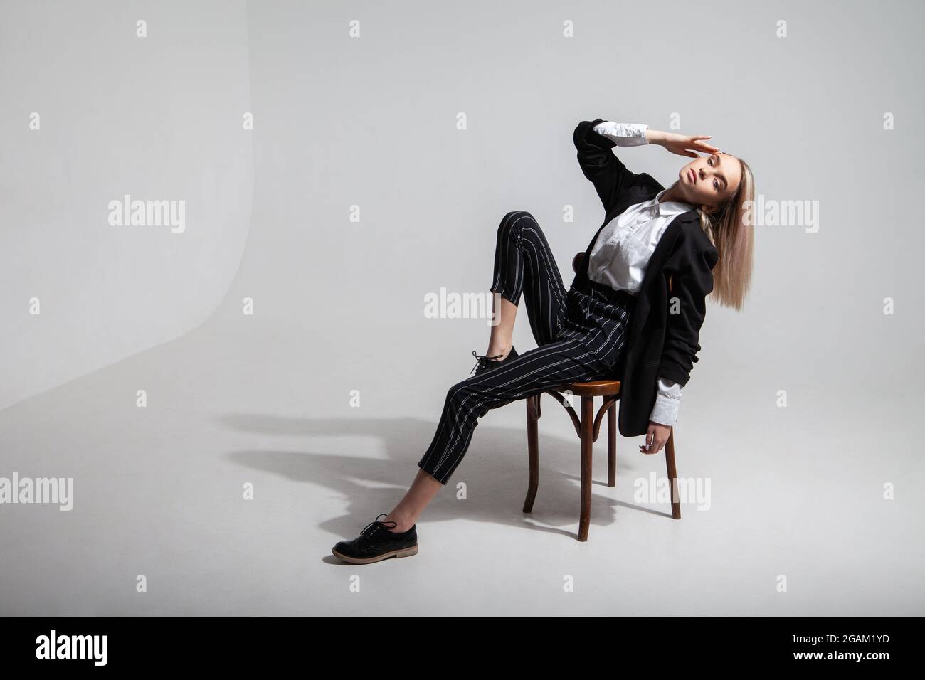Frau in stilvollem Outfit sitzt auf einem Stuhl Stockfoto