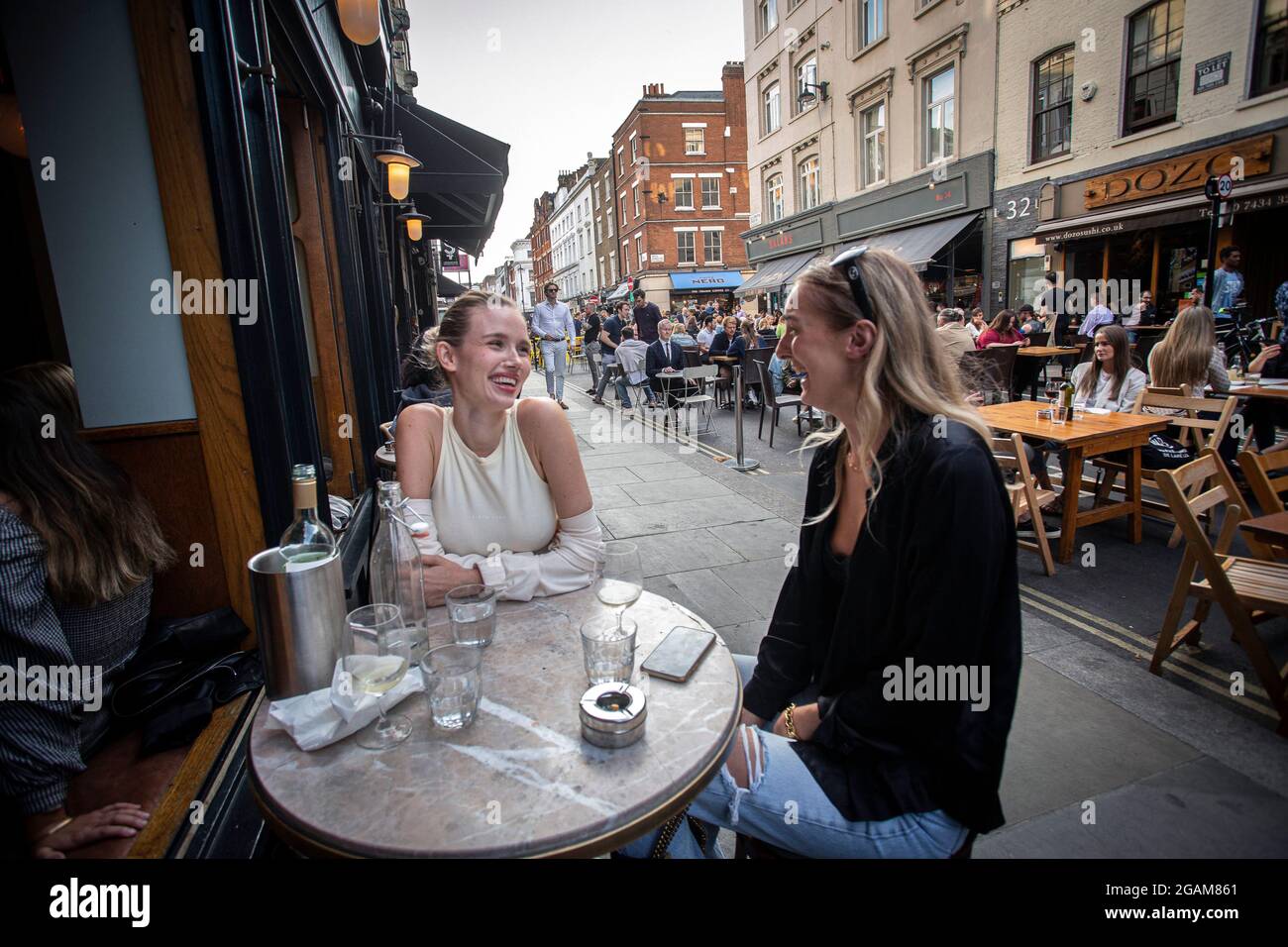 Zwei junge Frauen, die den „Tag der Freiheit“ feiern, der über ein Jahr der COVID-19-Sperrbeschränkungen endet in England, wo Menschen auf Tischen außerhalb der Stadt trinken Stockfoto