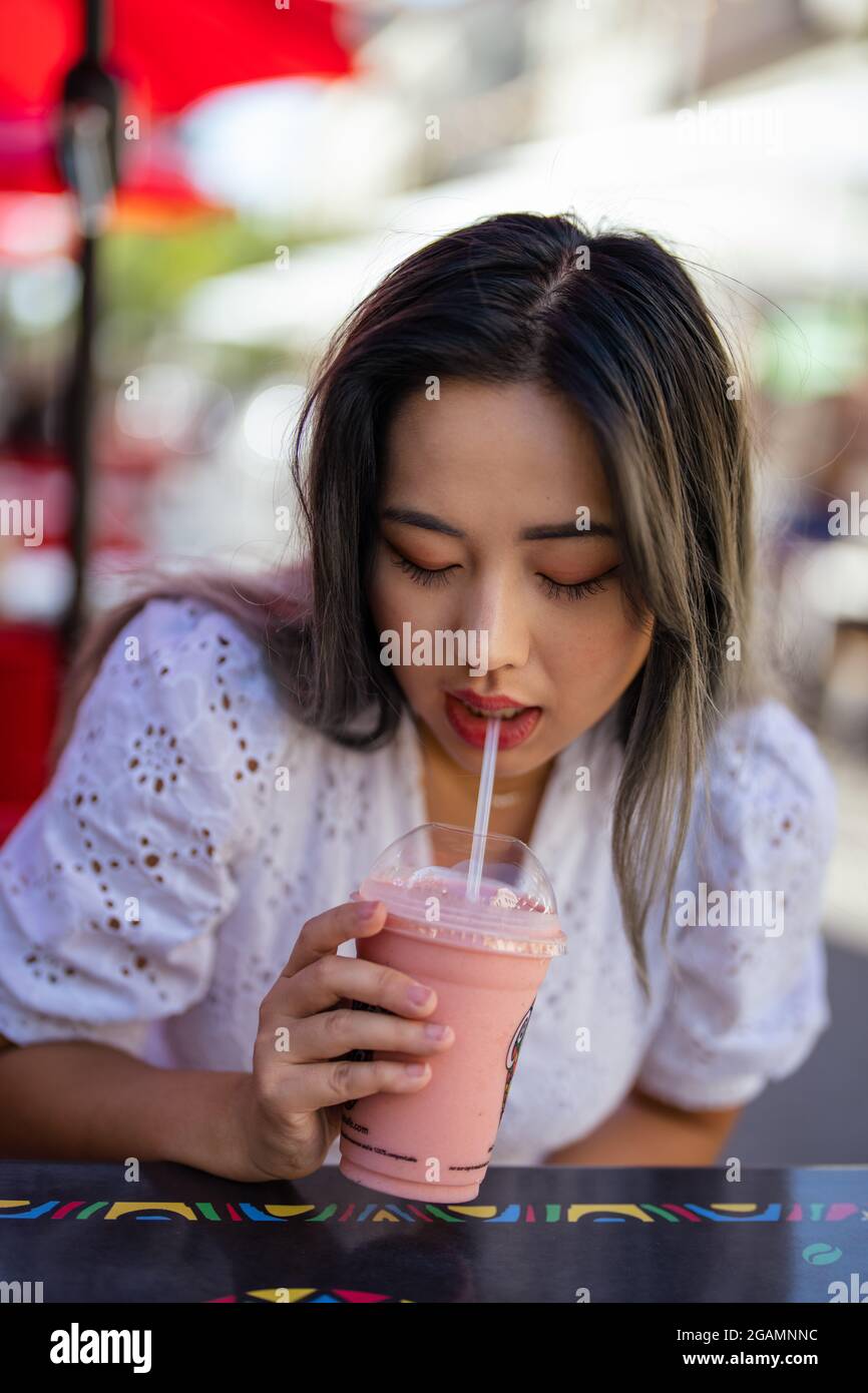 Schöne asiatische Frau trinkt einen Erdbeer Smoothie Stockfoto