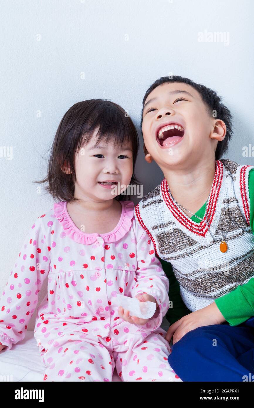 Kleine asiatische (thailändische) Kinder glücklich, Bruder lachend und Schwester lächelnd auf weißem Wandhintergrund, konzeptuelles Bild über die Liebe und Bindung von sibli Stockfoto