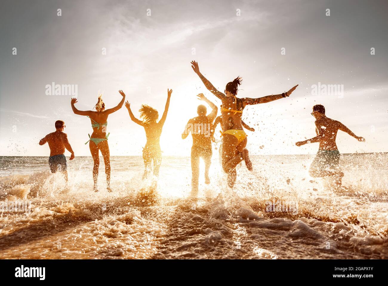 Eine große Gruppe von Freunden läuft und springt am Sunset Sea Beach. Sommerferien Konzept Stockfoto