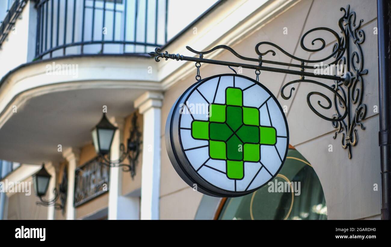 Ein Zeichen einer Apotheke an der Wand eines Hauses auf einer Stadtstraße. Grünes Symbol des Apothekenkreuzes. Stockfoto