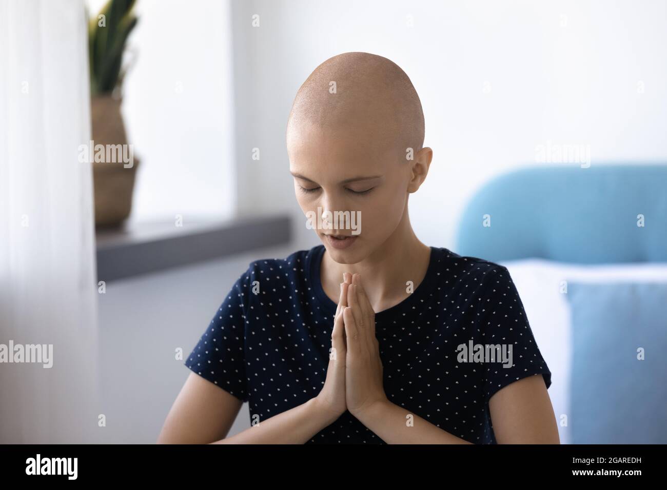 Glückliche junge haarlose Frau, die mit gefalteten Händen betet. Stockfoto