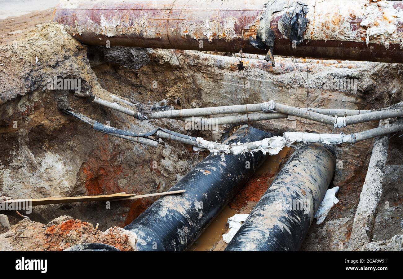 Reparatur des Heizkanals. Große Eisenrohre in einer Tiefe des ausgegrabenen Grabens. Stockfoto