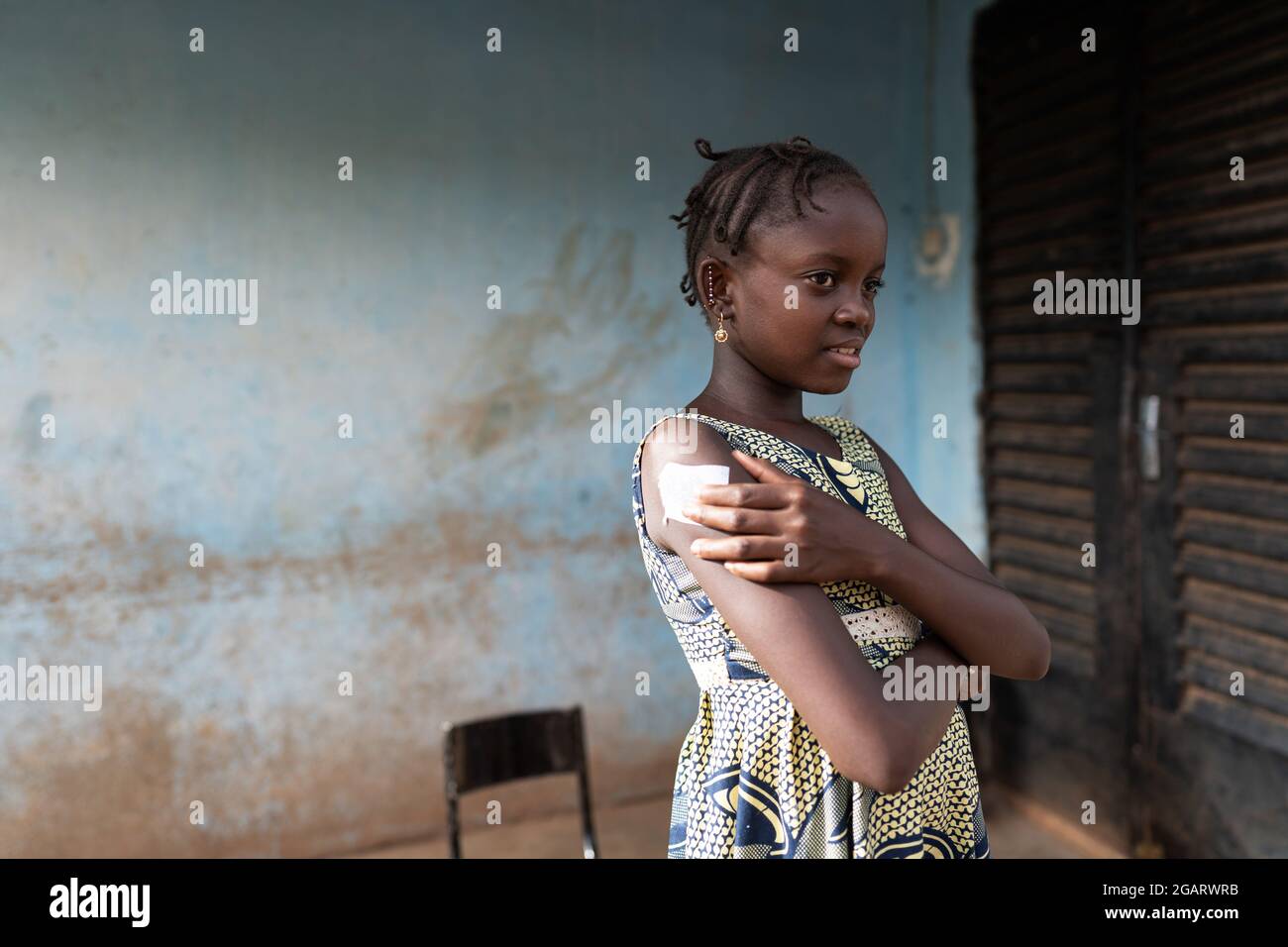 Auf diesem Bild drückt ein lächelndes, kleines afrikanisches Mädchen mit einem erleichterten Gesichtsausdruck ein saugfähiges Wattestäbchen auf die Injekton-Stelle Stockfoto